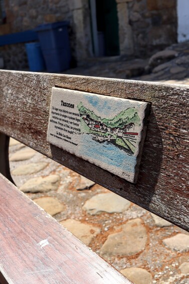 A wooden bench with a plaque that has text and a drawing of a coastal scene. 5