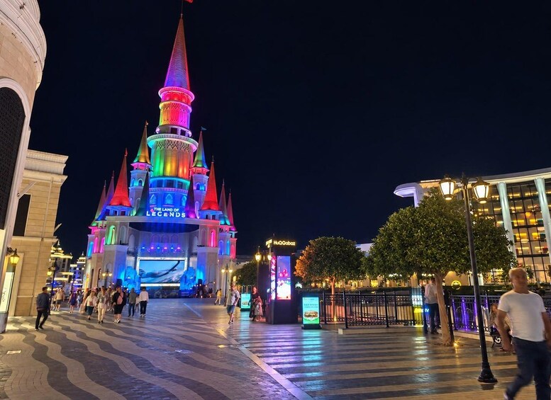 A brightly lit castle with a pointed spire, surrounded by a paved walkway and trees. 4