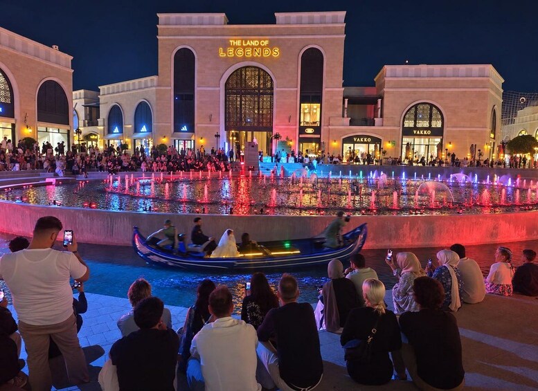 A nighttime scene with a water fountain show, a boat with people, and a building with illuminated signage. 3