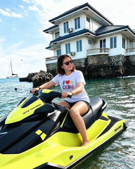 Eine Person fährt mit einem gelben Sea-Doo Jet-Ski auf ruhigem Wasser, im Hintergrund ein großes Haus und eine felsige Küstenlinie. 2
