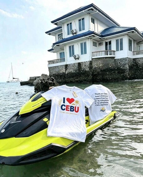 Ein gelbes Jetski mit zwei weißen T-Shirts, ein Haus am Wasser und ein Segelboot im Hintergrund. 1