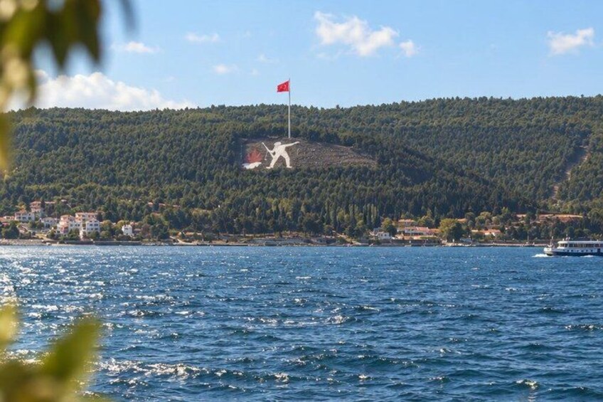 A lake with a red flag on a hill, a boat on the water, and a forested hill in the background. 5