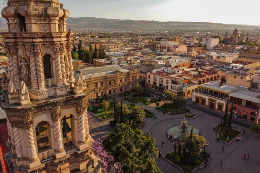 A historic tower, a central plaza with a fountain, and surrounding buildings. 2