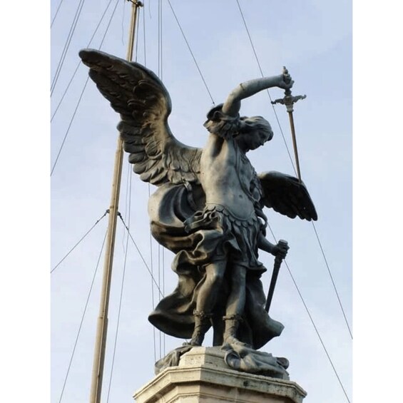 En statue af en engel med vinger, der holder et spyd og står på en fod 4