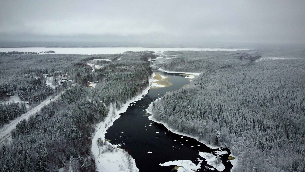 Une rivière serpente à travers une zone densément boisée, où les arbres sont couverts de neige et le ciel est nuageux. 4