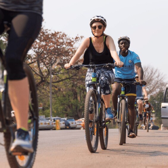 People riding bicycles on a paved path with trees and parked cars in the background. 5