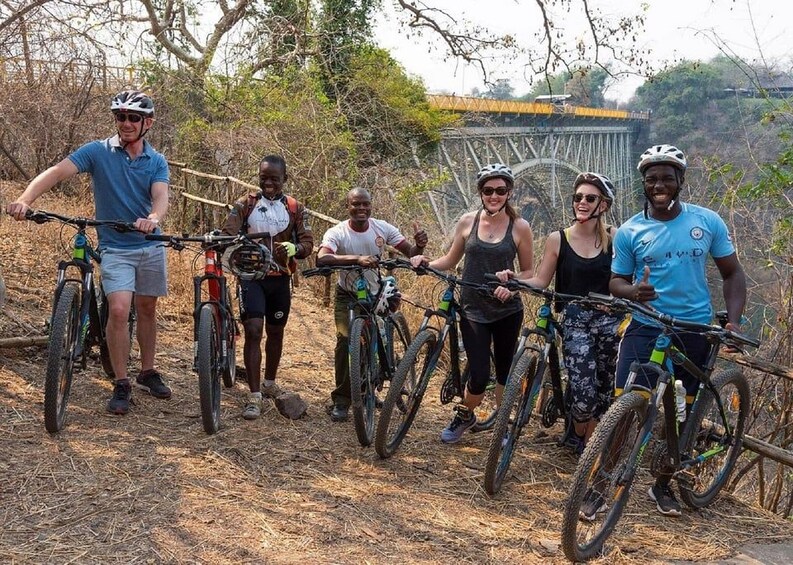 A group of people on bicycles in a natural setting with a bridge in the background. 1
