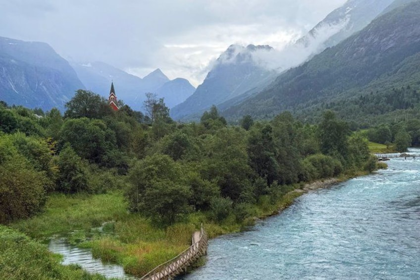 A river, a wooden bridge, and a church in a mountainous landscape. 2