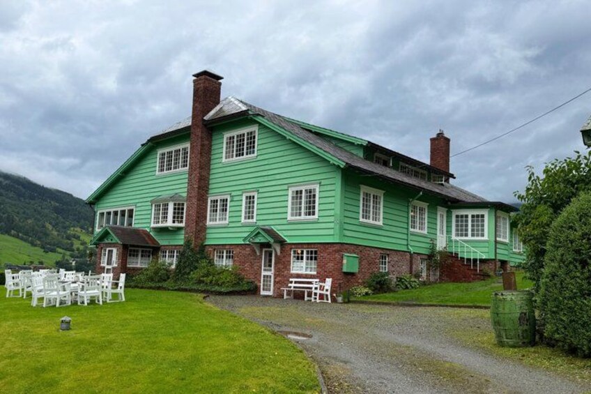 A green house with a brick chimney, surrounded by a grassy lawn and a gravel path. 3