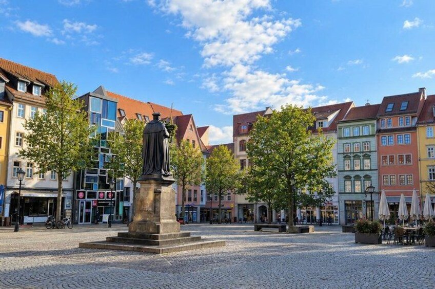 A cobblestone square with a statue, colorful buildings, and trees. 4