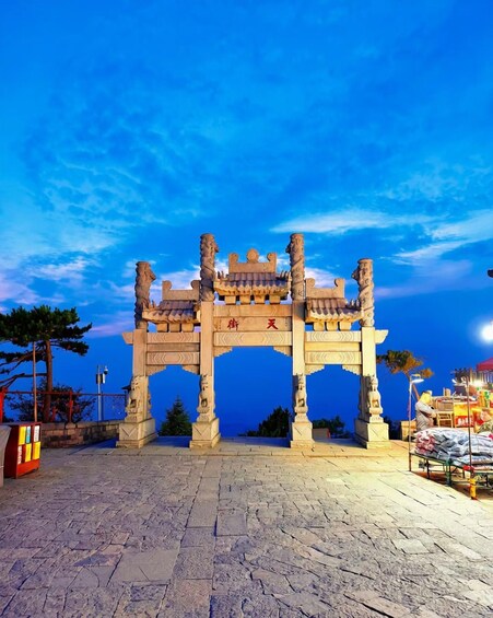 A stone archway with intricate carvings and a red inscription, set against a twilight sky. 1