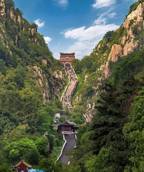 A mountain path leading to a temple with a red roof, surrounded by lush greenery and rocky cliffs. 2
