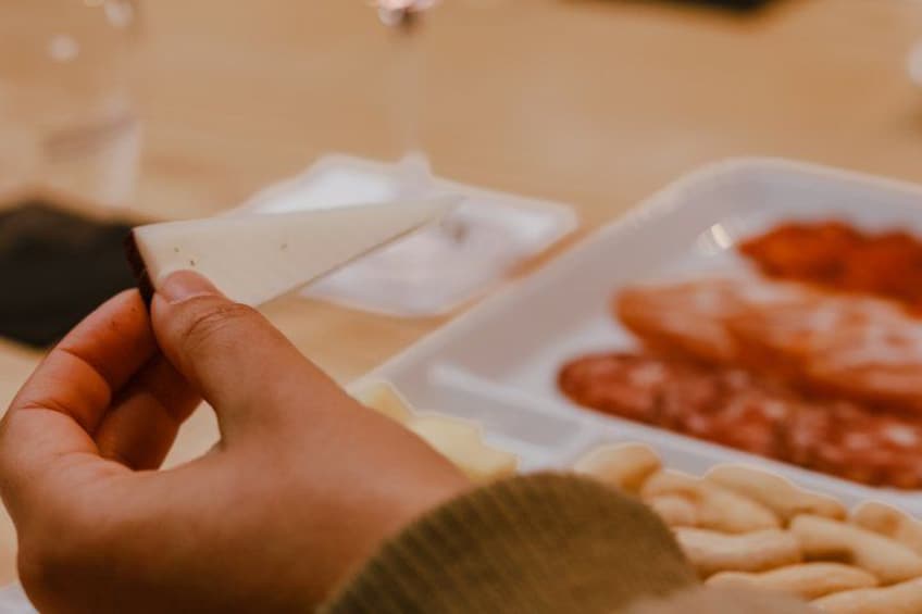 A hand holding a piece of bread, with a plate of pasta and a glass of water in the background. 3