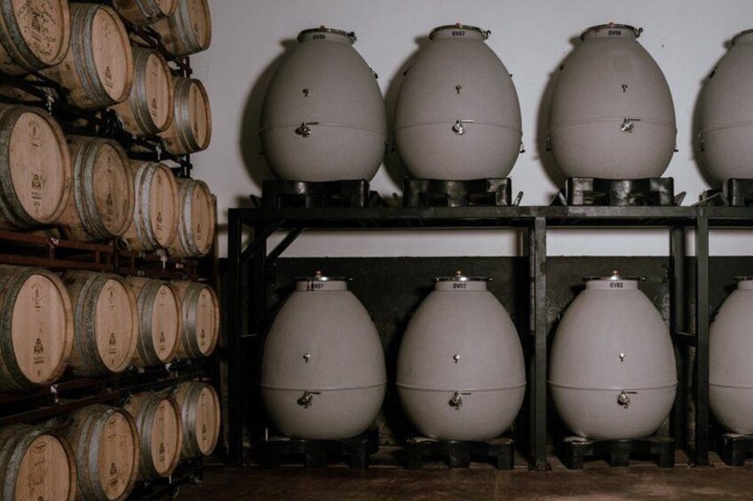 Wooden barrels stacked against a wall, with large white containers on shelves below. 5