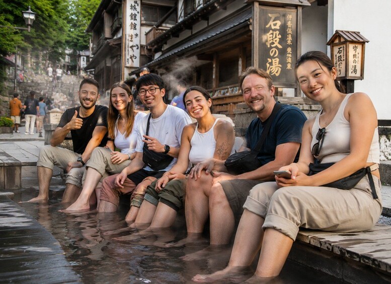 A group of people sitting on a stone platform in a hot spring area with traditional Japanese architecture in the background. 4