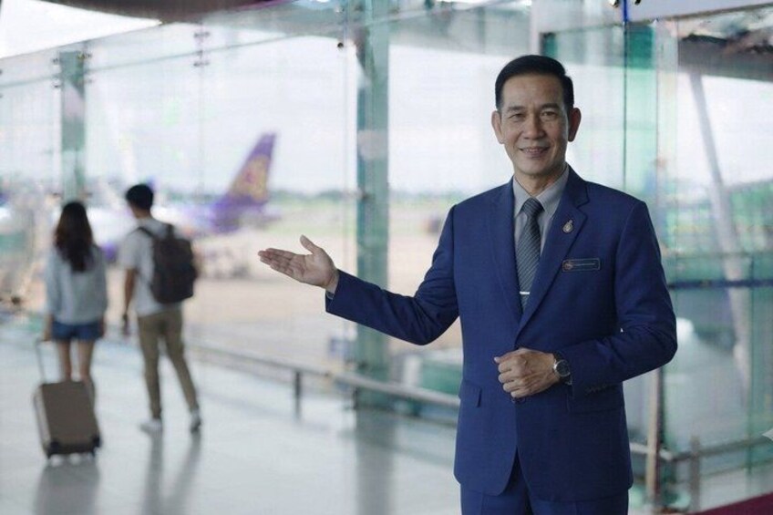 A man in a blue suit standing in an airport terminal with a glass wall and a plane visible in the background. 4