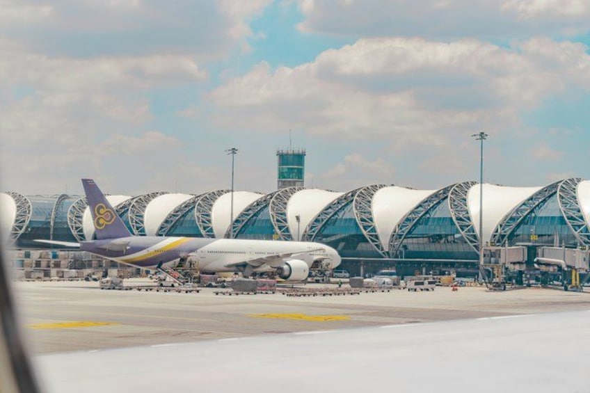 An airport with a distinctive modern terminal featuring curved, white roofs and a parked airplane. 5