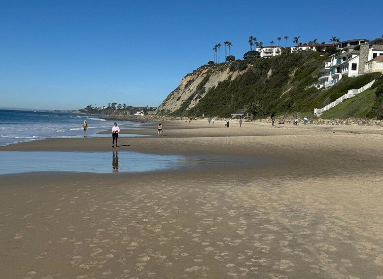 A sandy beach with footprints, a clear sky, and houses on a hillside. 4