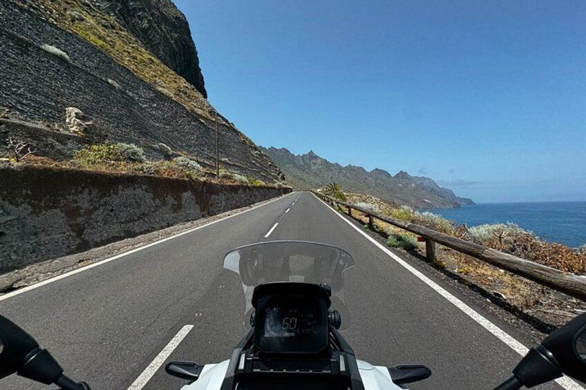 A motorcycle on a coastal road with a clear sky and ocean in the background. 2