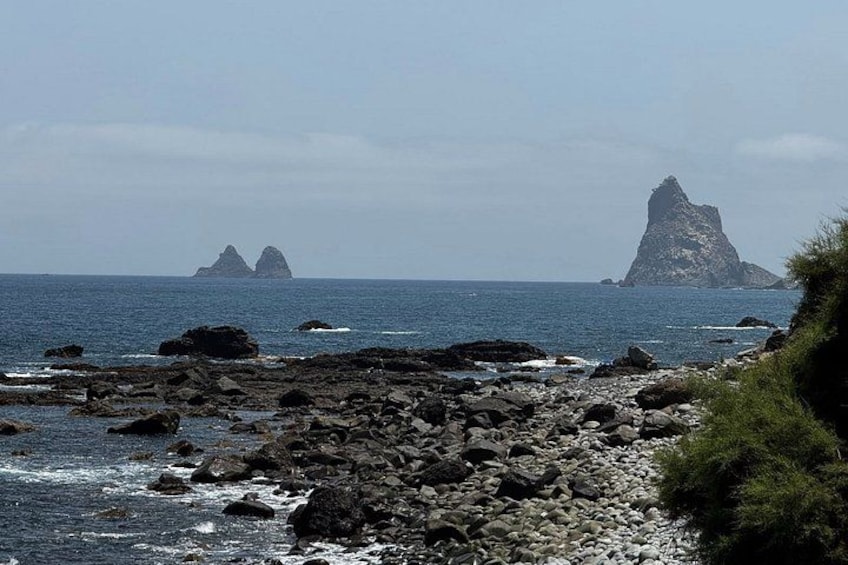A rocky shoreline with waves, distant islands, and a clear sky. 3