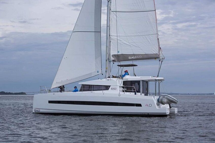 A white catamaran with the name 'BALI' on its side, sailing on calm waters. 1