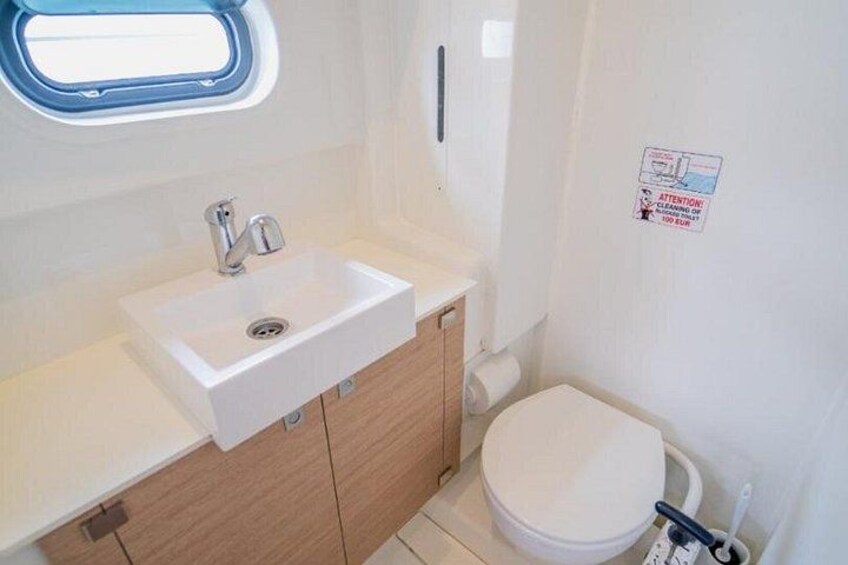 A small bathroom with a white sink, wooden cabinets, a toilet, and a window. 2