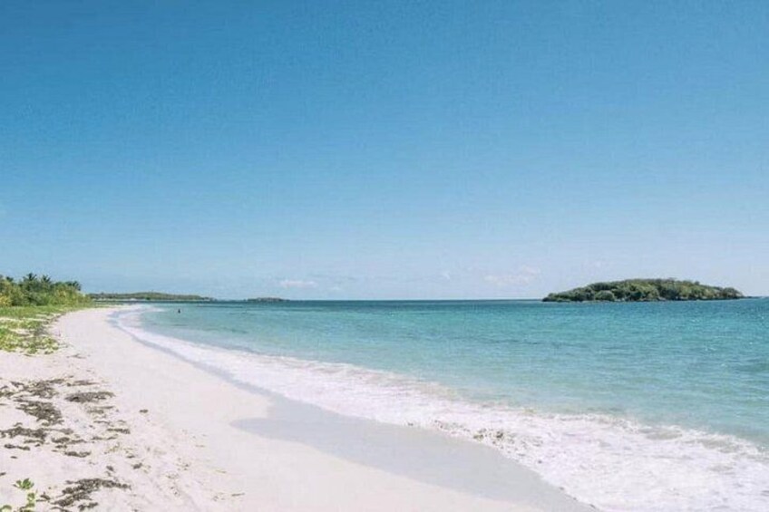 A beach with white sand, clear turquoise water, and a small island in the distance. 5