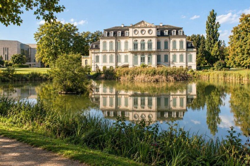 A large classical building with a reflection in a pond, surrounded by greenery and trees. 5
