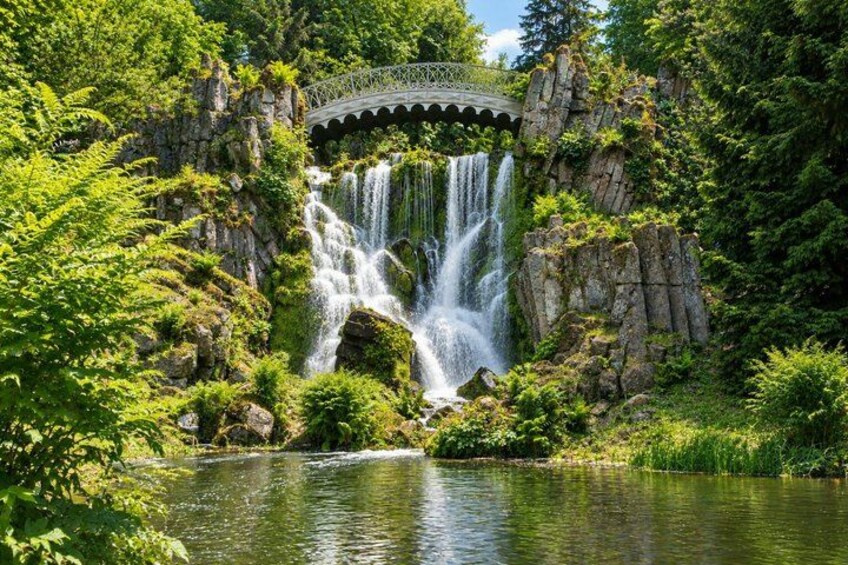 A waterfall cascading over rocks, surrounded by lush greenery and a bridge. 4