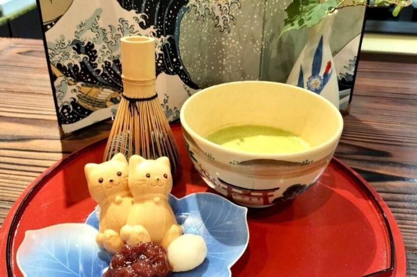 A traditional Japanese tea set with a whisk, a bowl, and a decorative cat-shaped container on a red tray. 3