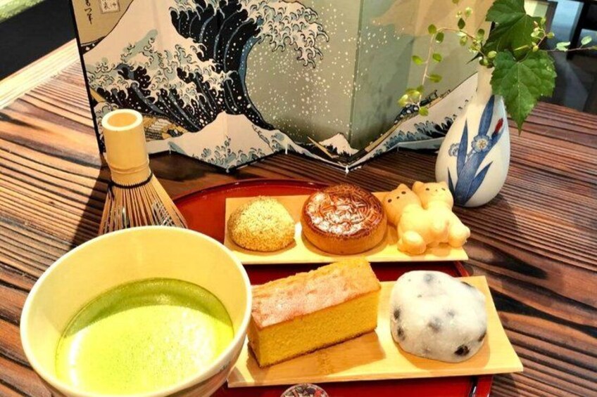 A traditional Japanese tea ceremony setup with a tea bowl, a whisk, and a tray with sweets and a cake. 2