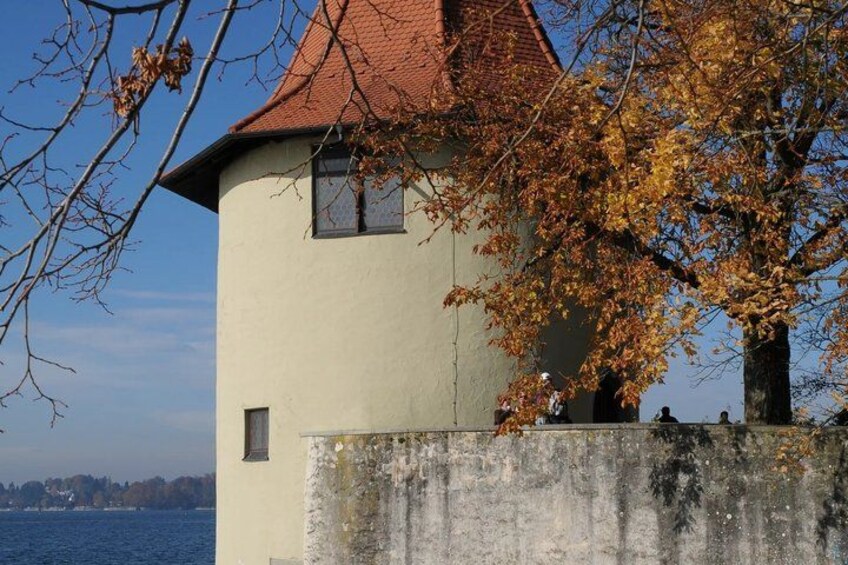 A tower with a red roof, a beige wall, and a tree with autumn leaves. 4