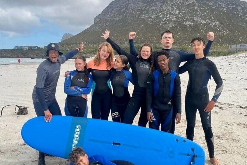 A group of people in wetsuits on a beach with a surfboard. 2