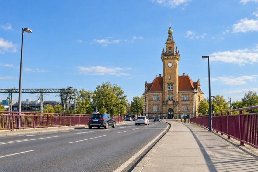 A road with vehicles, a pedestrian bridge, and a large building with a clock tower. 4