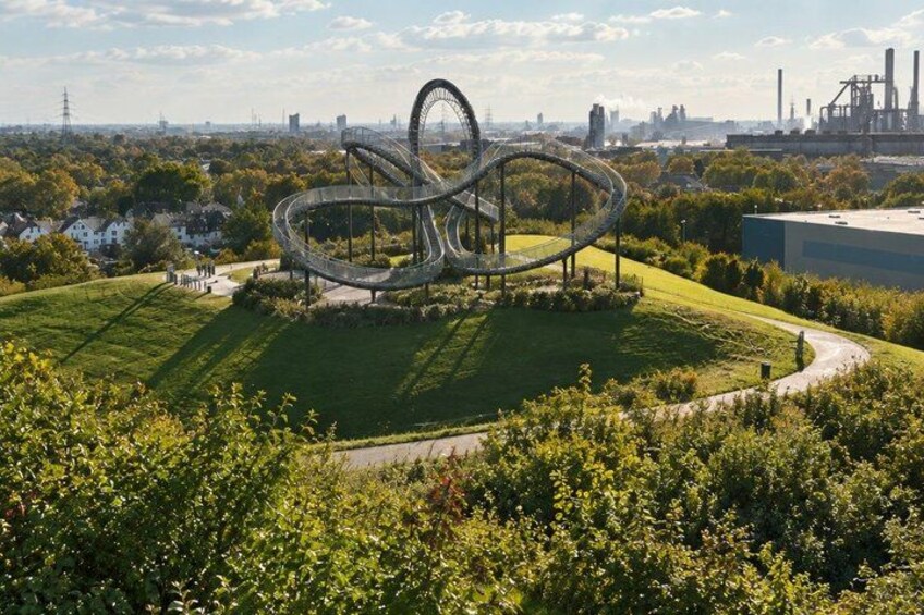 A large spiral sculpture in a park with a cityscape in the background. 4