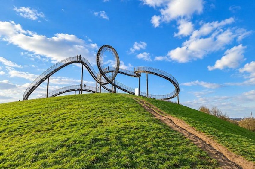 A roller coaster on a grassy hill with a clear blue sky. 3