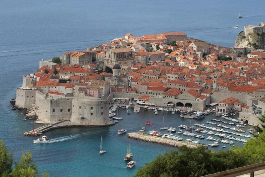 A coastal town with historic buildings, a fortified castle, and a marina with boats. 5