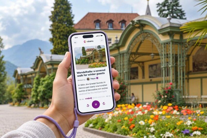 A person holding a smartphone displaying a photo of a covered walkway with colorful flowers in the background. 1