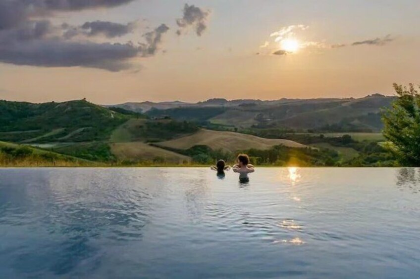A serene pool with two people enjoying the view of rolling hills and a sunset. 5