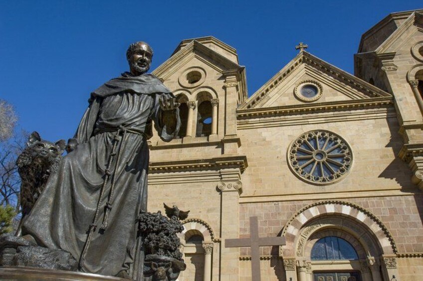 A statue of a robed figure in front of a church with a large circular window and a cross on the facade. 3