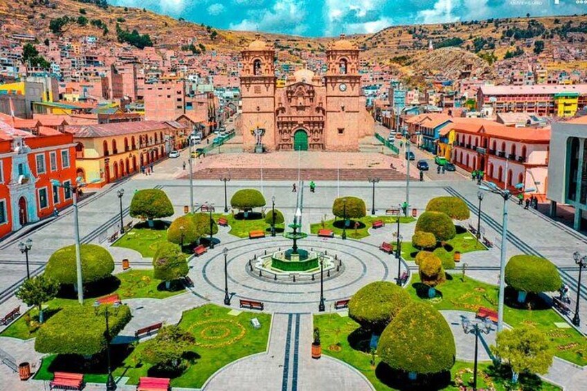 A plaza with a central fountain, surrounded by trimmed hedges and a historic building with a clock tower. 1