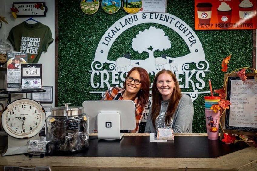 Two people at a counter with a green backdrop, a clock, and various items on the counter. 4