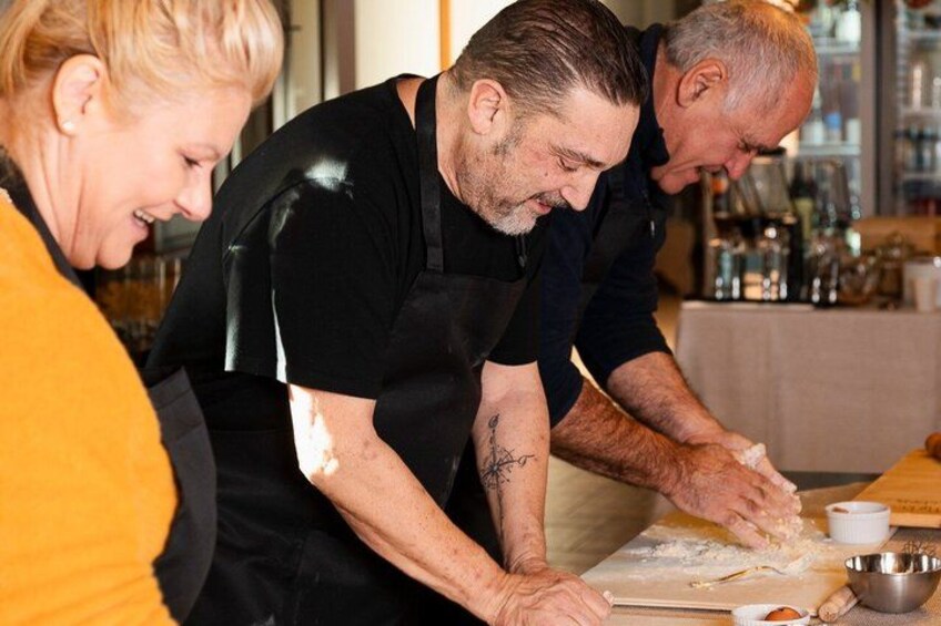 Three people preparing food, with a table covered in flour and kitchen utensils. 2
