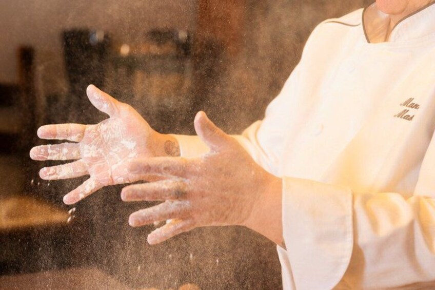 A person in a white chef's coat with a logo, handling flour. 5