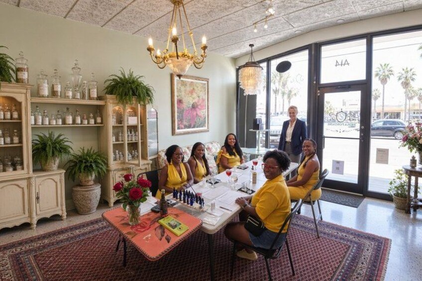 A group of people seated around a table in a well-lit room with a chandelier, potted plants, and a large window. 5