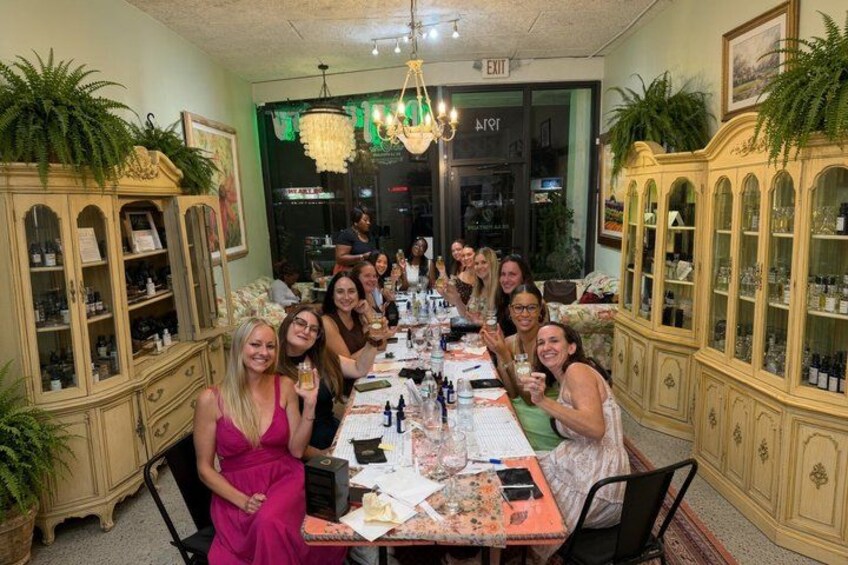 A group of people seated around a long table in a room with ornate cabinetry and a chandelier. 1