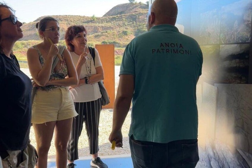 A group of people standing near a glass wall, looking at a landscape with hills in the background. 1