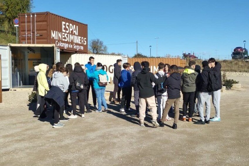 A group of people gathered around a building with a sign that reads 'ESPAI MINESIMINERS Calonge de Segura.' 4