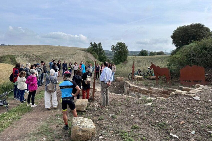 A group of people standing on a dirt path, a horse statue, and a bicycle. 3