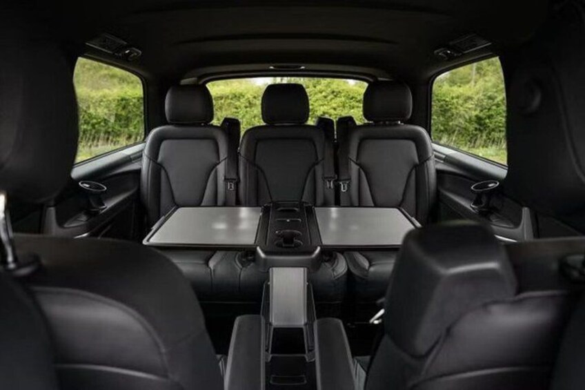 The interior of a car with a central table, black leather seats, and a sunroof. 2